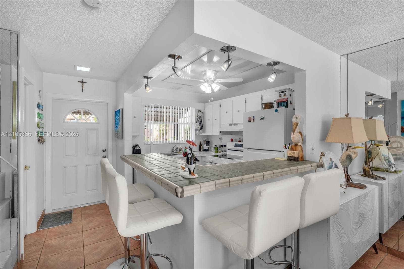 Kitchen featuring white cabinetry and appliances, tile flooring, and a breakfast bar with tile countertop
