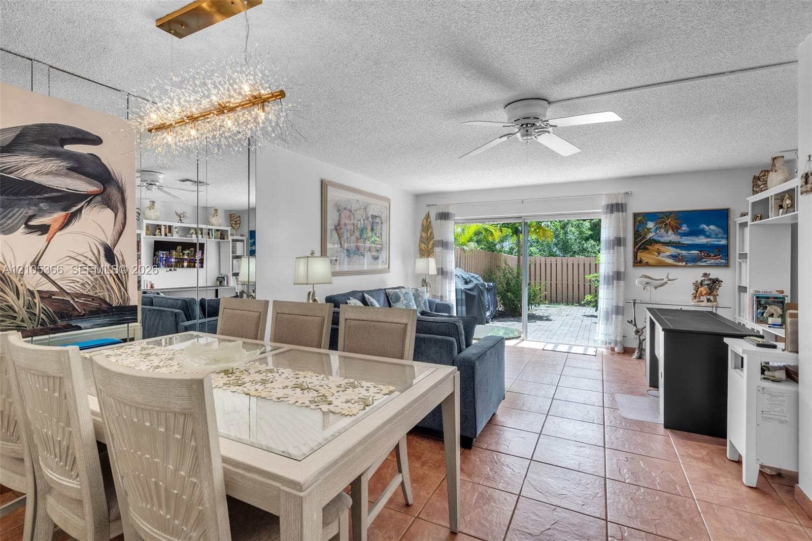Open-concept living space with tile flooring throughout, a modern chandelier, and sliding glass doors leading to an outdoor patio