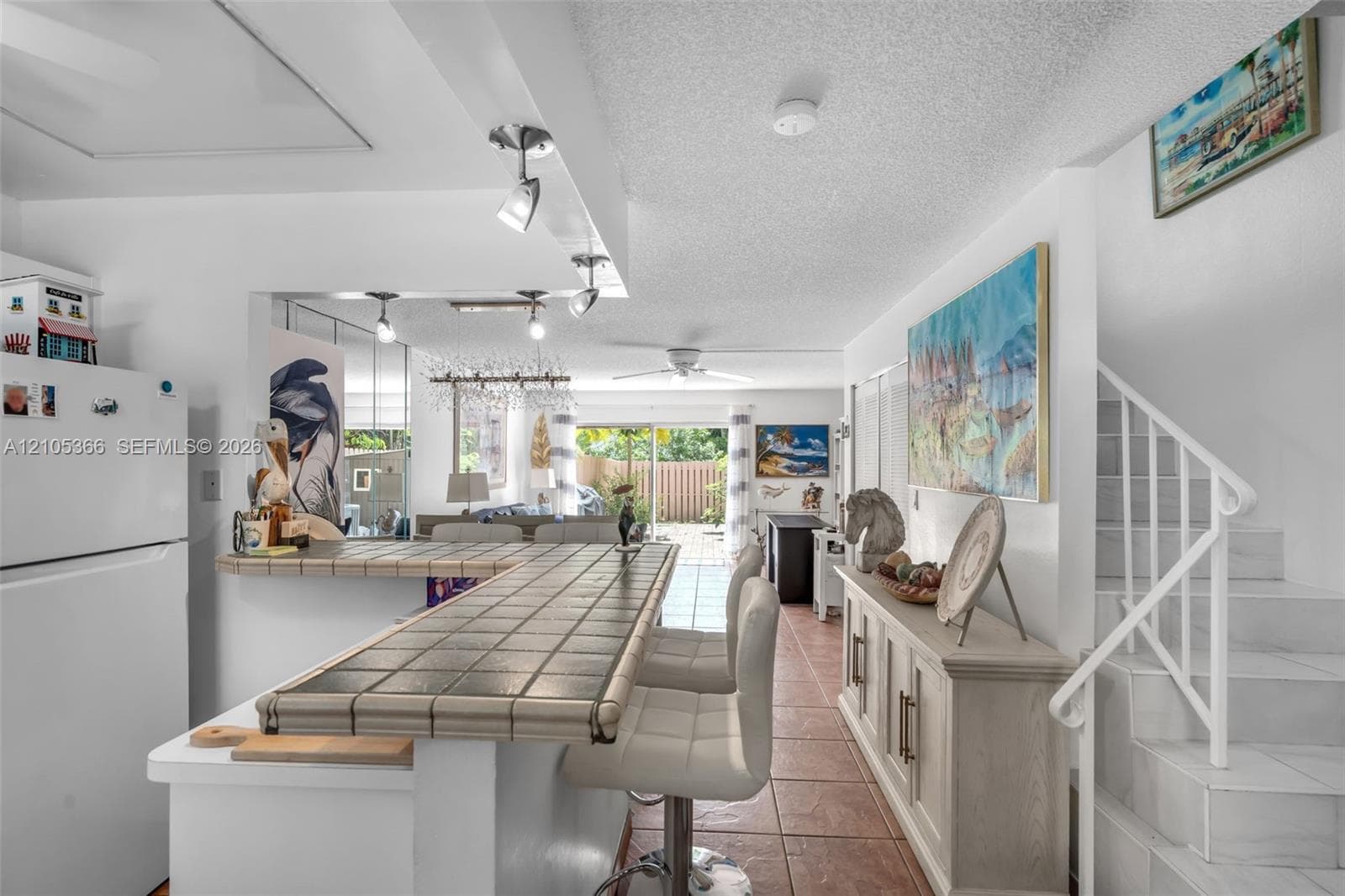 Tiled kitchen counter with a breakfast bar, white appliances, and track lighting