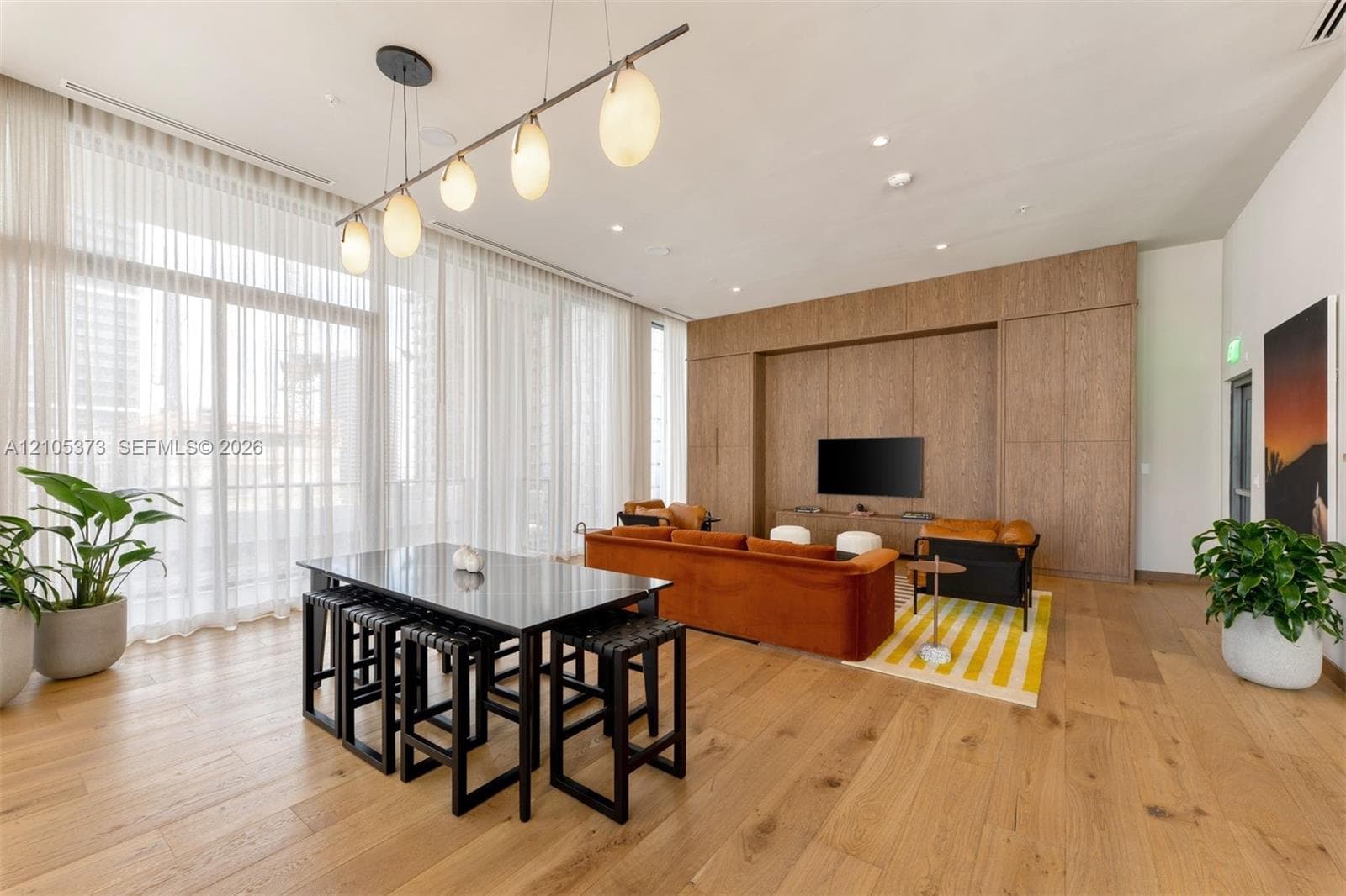 Expansive windows with sheer drapery, wood-finish flooring, recessed lighting, and a built-in media wall with wood paneling