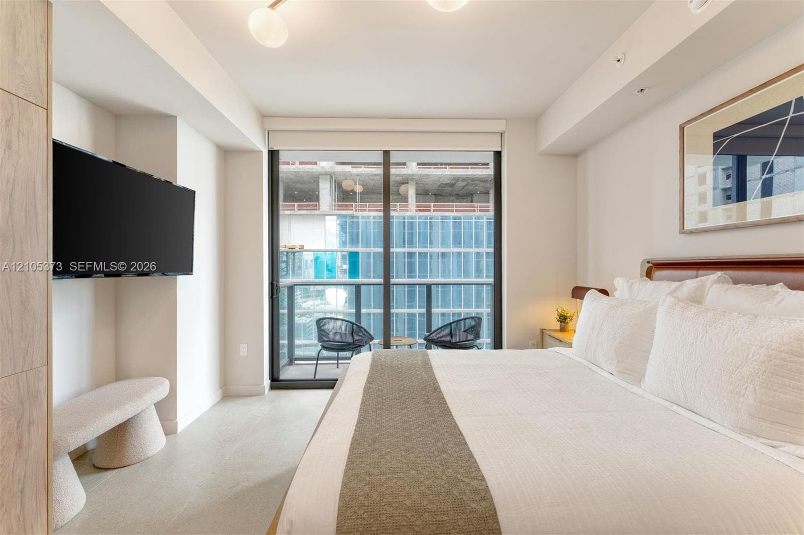 Floor-to-ceiling glass door leading to a private balcony, featuring a wall-mounted television, recessed lighting, and a contemporary ceiling fixture