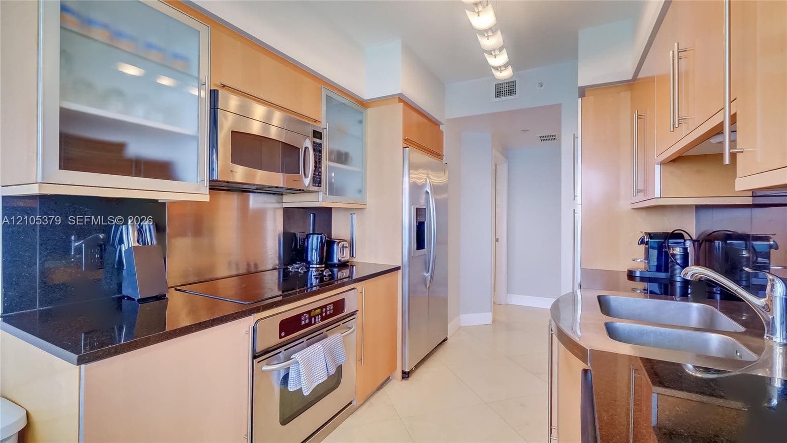 Stainless steel appliances, black countertops, wood-finish cabinetry, under-cabinet lighting, and a double-basin sink