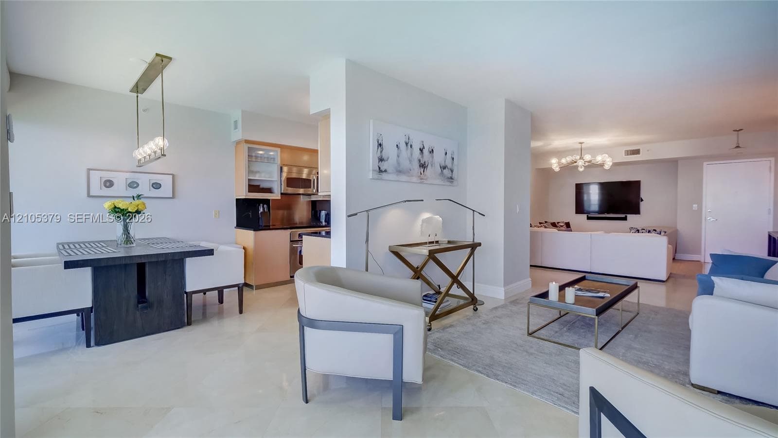 Open-concept living area with light-toned flooring, a dining area featuring a linear pendant light fixture, and a kitchen with wood-finish cabinetry and stainless steel appliances