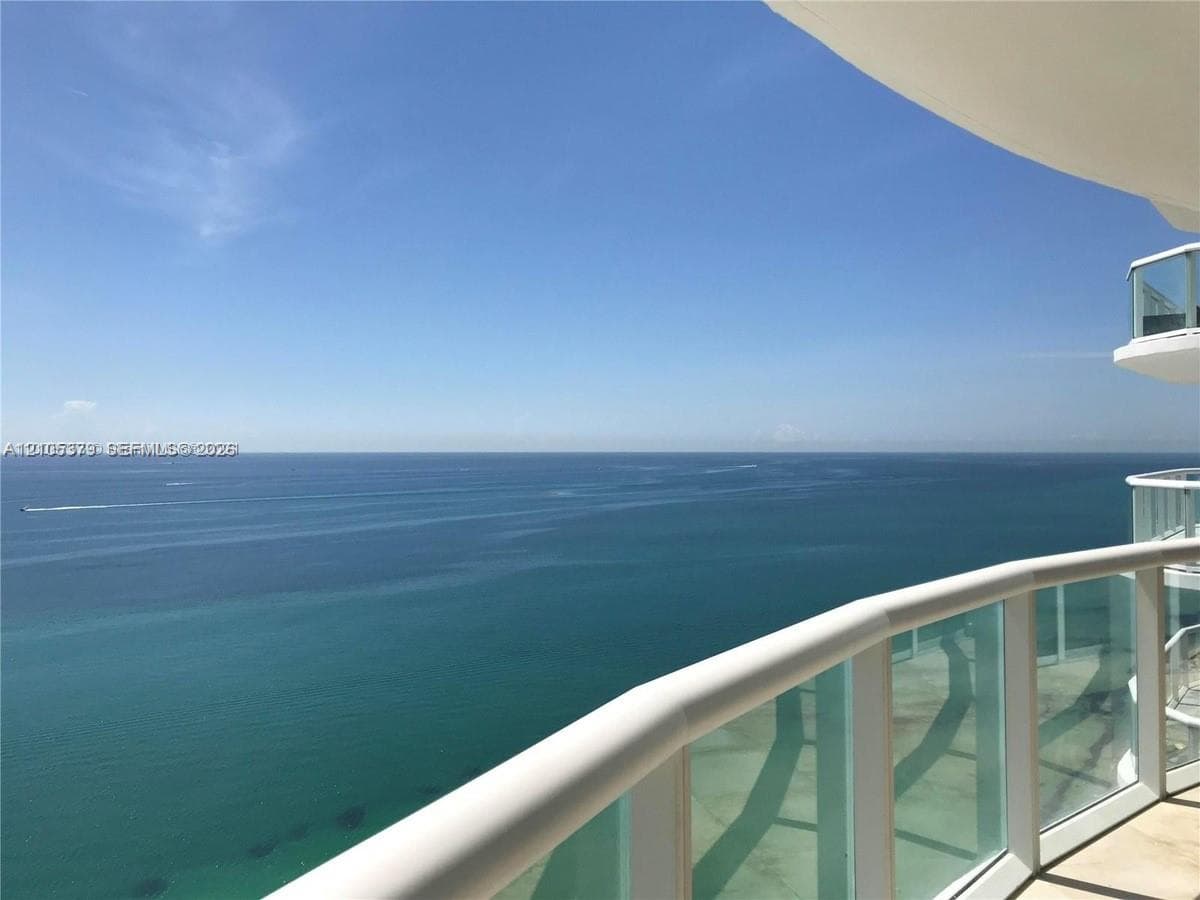 Expansive ocean backdrop with a clear horizon, featuring a curved balcony with a glass and white railing