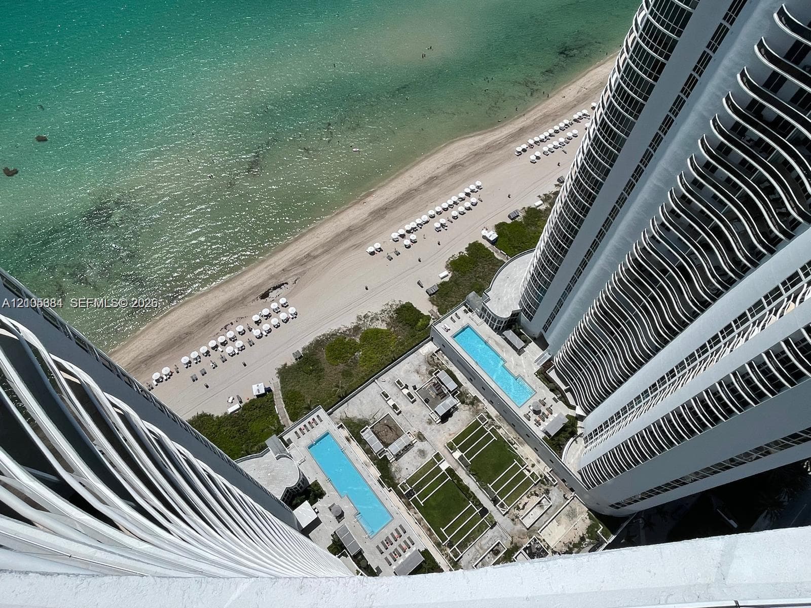 Oceanfront property featuring two outdoor swimming pools, a sandy beach, and manicured green spaces