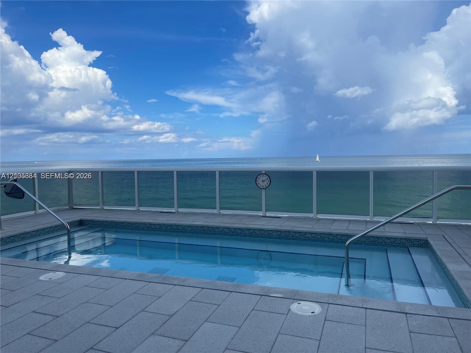 Private pool with integrated steps, surrounded by paver decking and a clear panel railing, all overlooking the ocean
