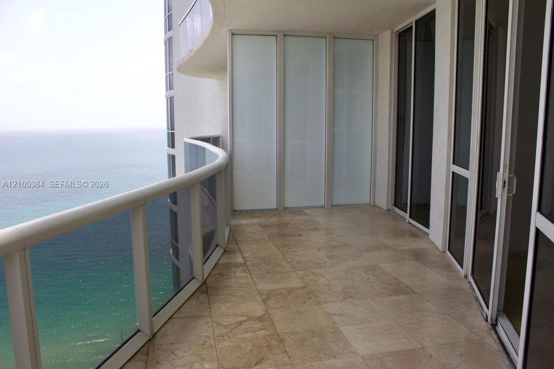 Curved balcony with glass railing, large format stone-finish tile flooring, and multiple glass sliding doors