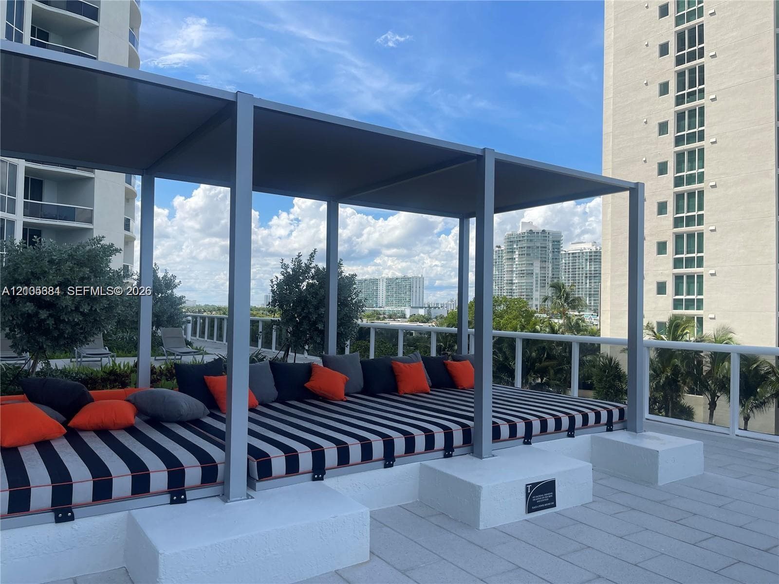 Rooftop terrace featuring a covered lounge area, glass panel railings, and urban skyline backdrop