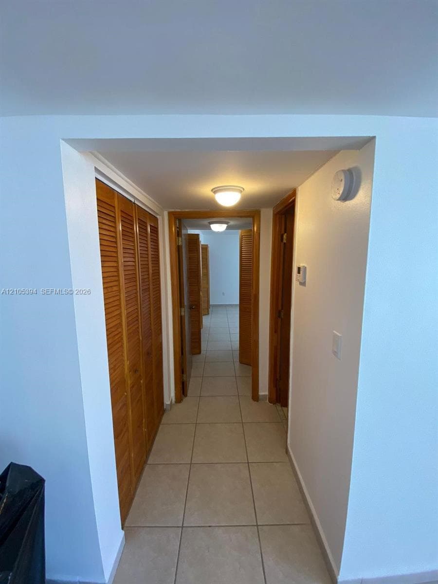 Hallway featuring tile flooring, flush mount lighting, and wood-finish doors