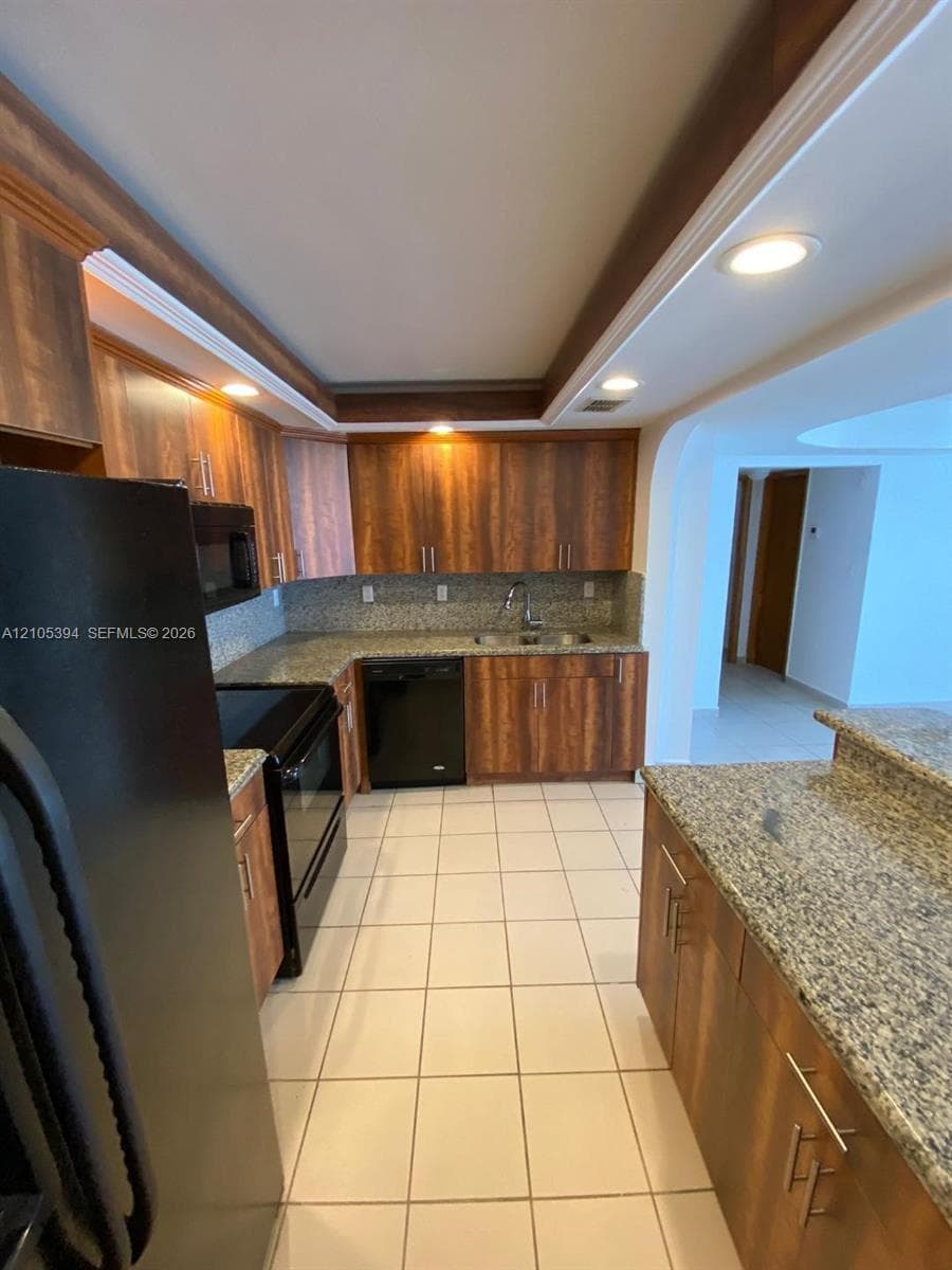 Full kitchen featuring wood-finish cabinetry, light-toned tile flooring, recessed lighting, and granite countertops
