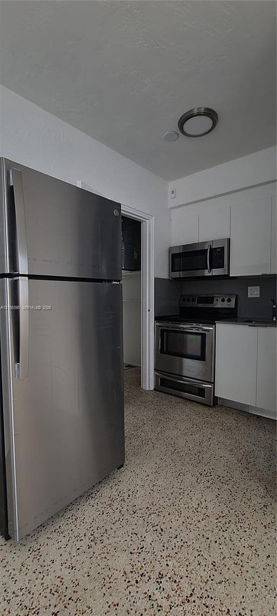 Stainless steel appliance suite, white flat-panel cabinetry, black countertops, and terrazzo flooring