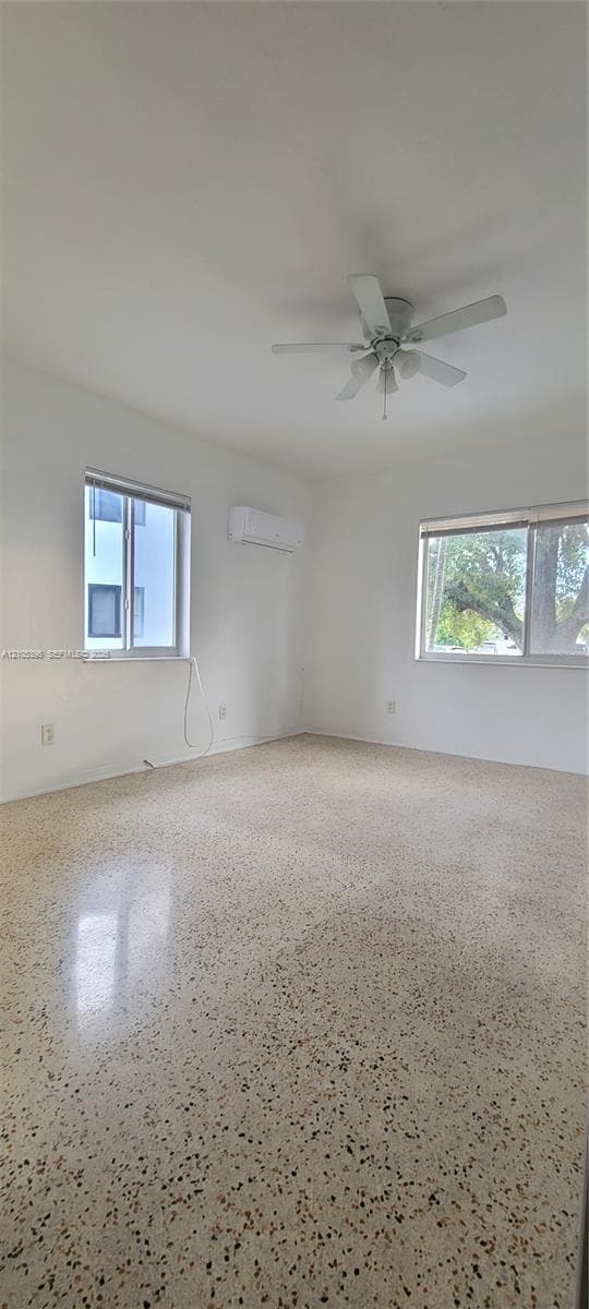 Polished terrazzo flooring, dual windows, ceiling fan, and wall-mounted air conditioning unit