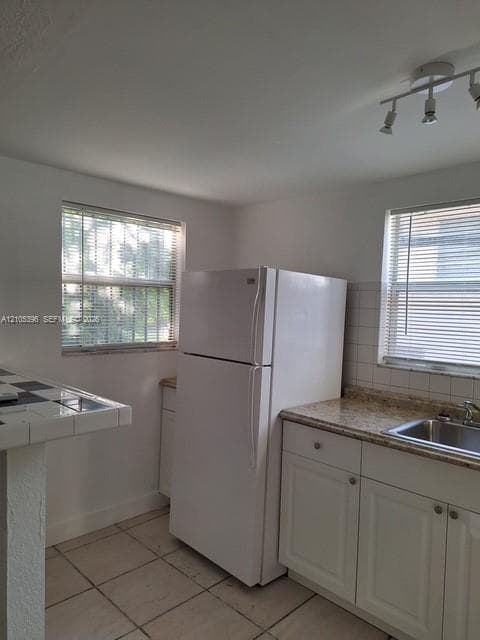 Tile flooring, white cabinetry, granite-finish countertops, stainless steel sink, and track lighting