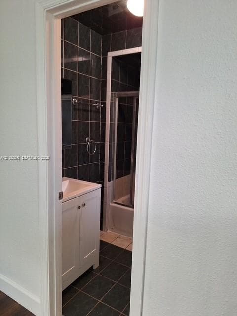 White vanity with dual doors and polished hardware, ceramic tile flooring, and dark tile shower surround with a sliding glass enclosure