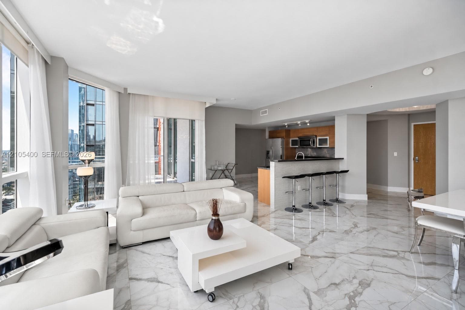 Expansive windows, high ceilings, large format marble-look tile flooring, and a kitchen featuring wood cabinetry with integrated appliances