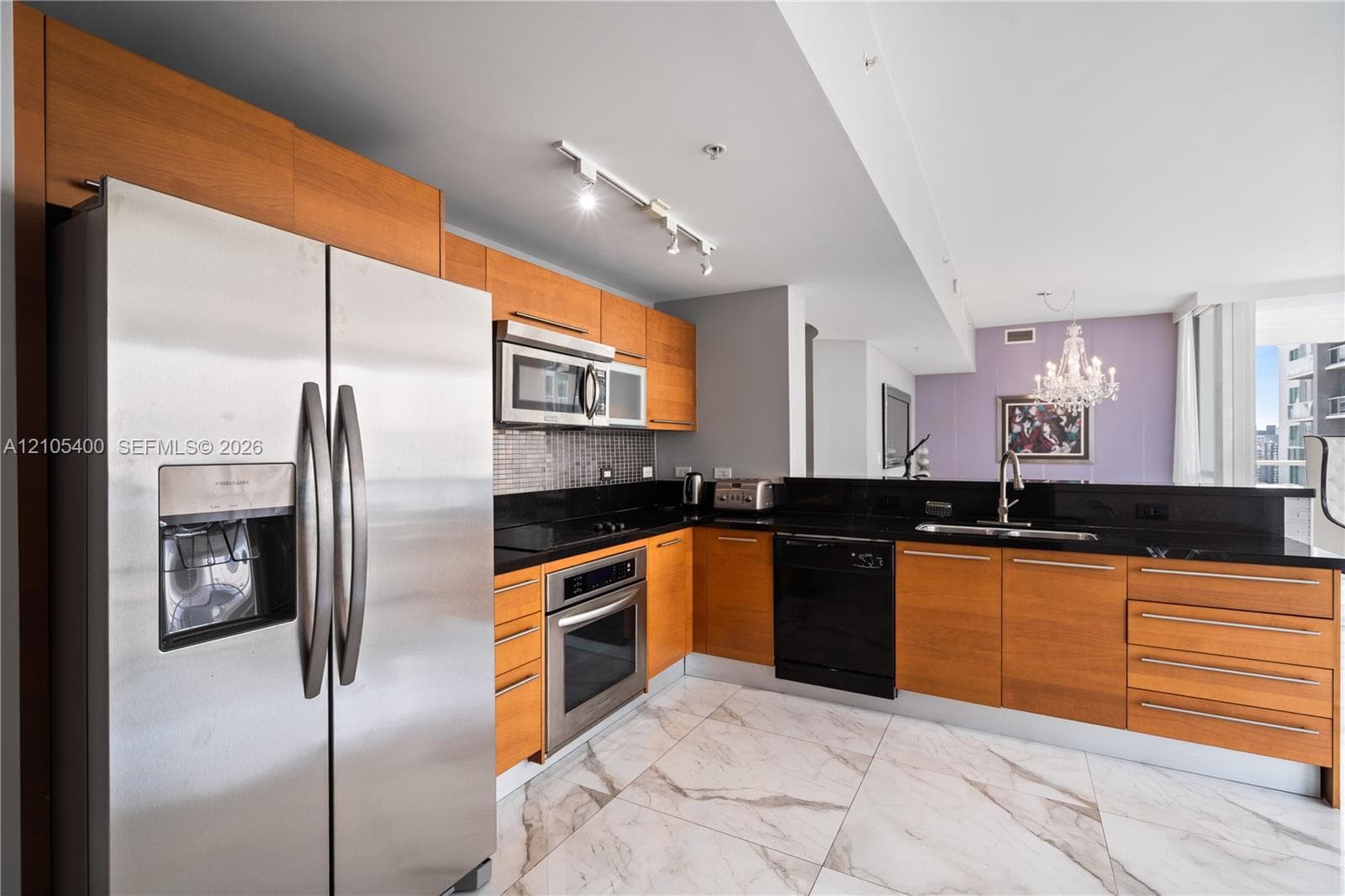 Kitchen featuring stainless steel appliances, wood-finish cabinetry, black countertops, and a tile backsplash