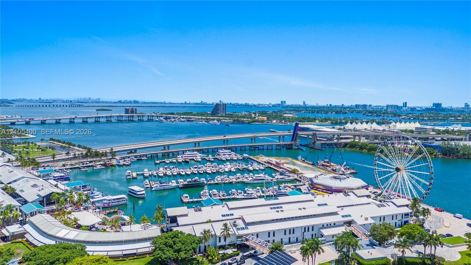 Aerial perspective showcasing a marina with numerous boats, multiple bridges crossing expansive blue water, and a prominent Ferris wheel