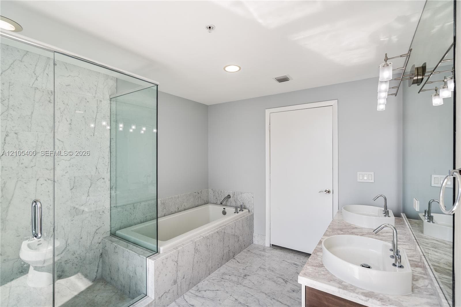 Glass-enclosed shower, built-in soaking tub, dual vessel sinks, full-width vanity mirror, and recessed lighting