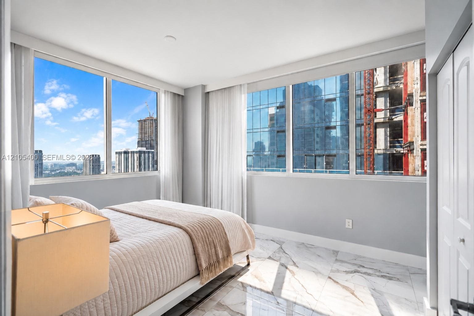 Floor-to-ceiling windows, white marble-look flooring, white interior walls, white bi-fold closet doors, and white window treatments
