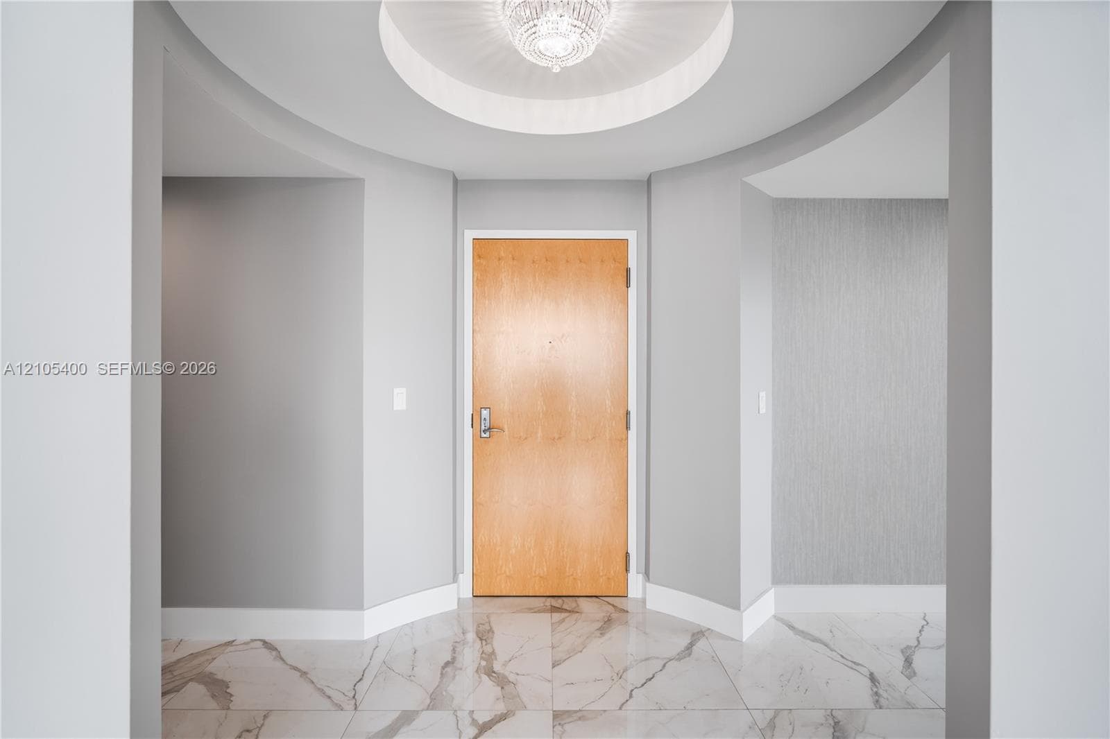Foyer featuring large format tile flooring, recessed ceiling with a central chandelier, and a wood entry door