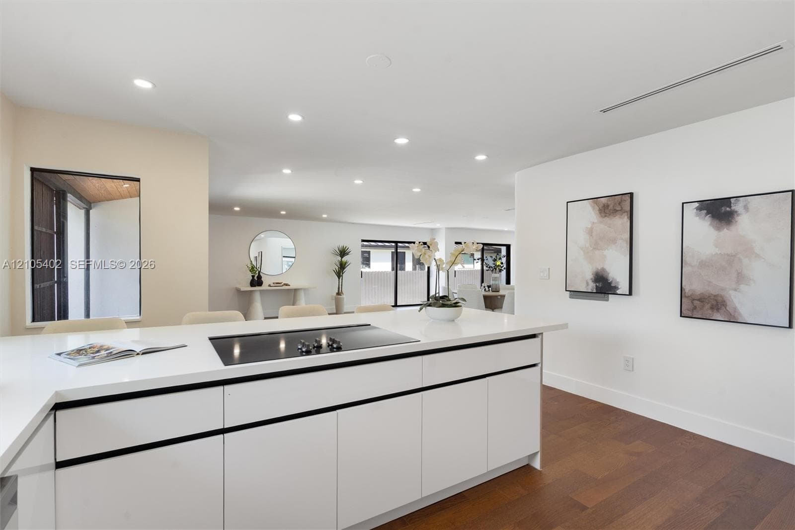 Kitchen island featuring white flat-panel cabinetry, a solid surface countertop, and an integrated cooktop, complemented by recessed lighting and wood-finish flooring