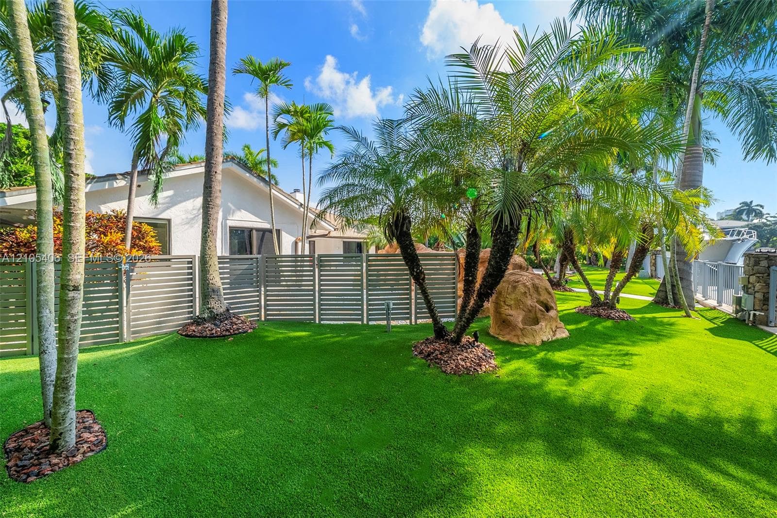 Expansive green lawn with mature palm trees, decorative rock formation, and privacy fencing