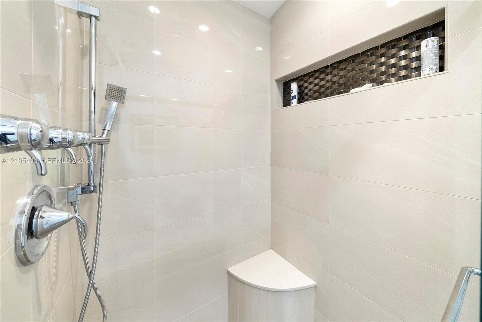 Shower with polished chrome fixtures, integrated niche with mosaic tile accent, a built-in corner bench, and large format wall tiling