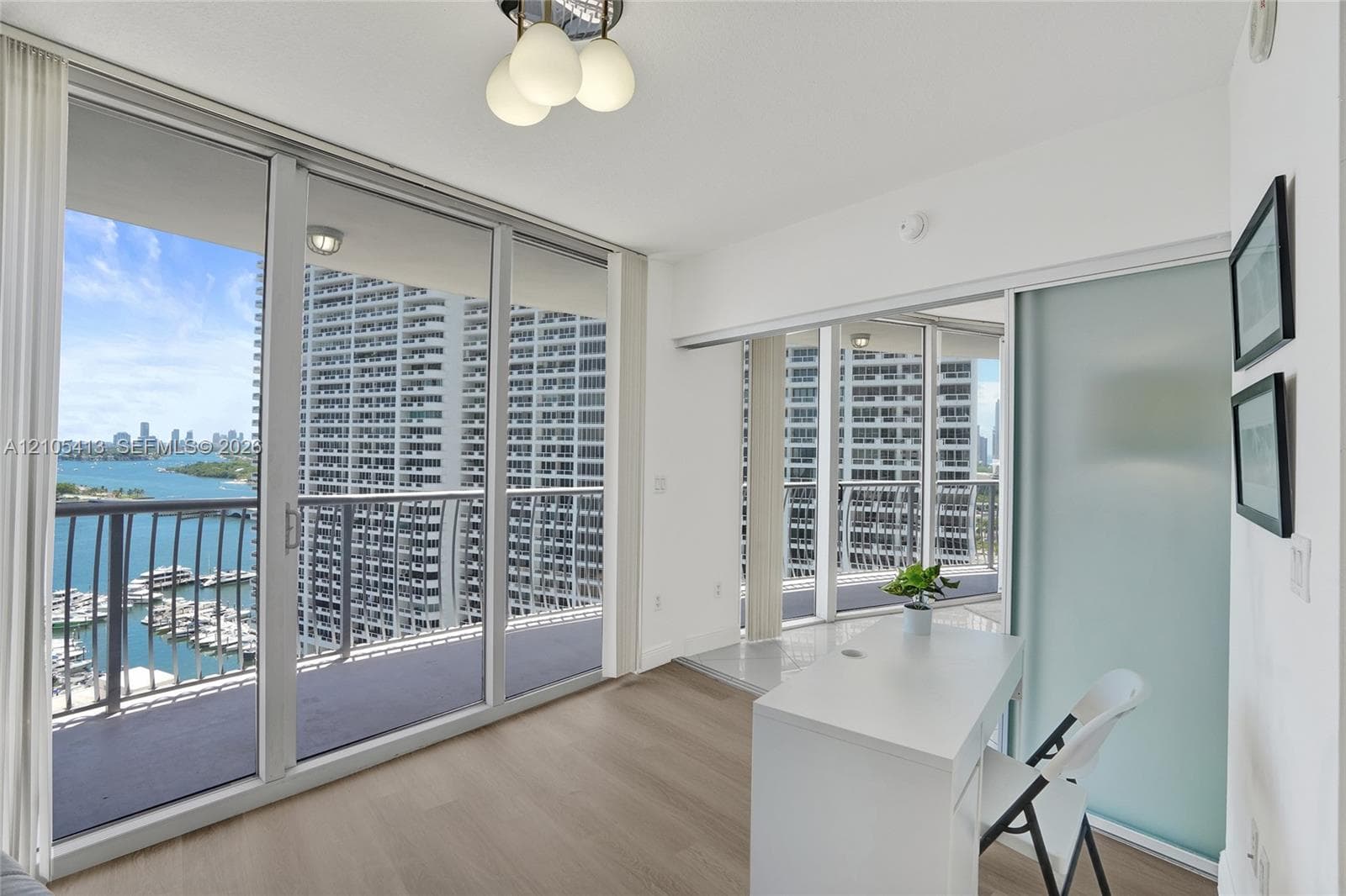 Expansive floor-to-ceiling glass sliding doors, private balcony with metal railings, wood-finish flooring, built-in counter surface, and a frosted glass sliding door