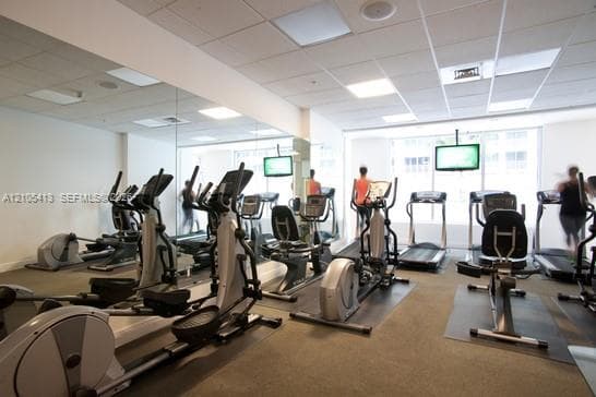 Fitness center with mirrored wall, multiple cardio machines, mounted flat-screen displays, and recessed lighting