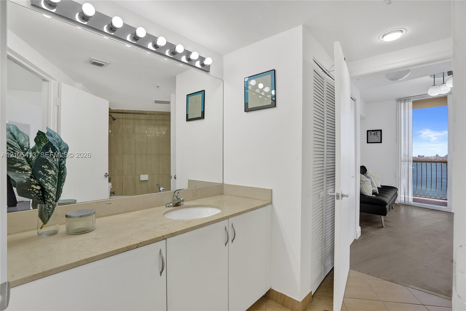 Vanity with an integrated sink and light-toned countertop, mirrored wall, vanity lighting, and white cabinetry