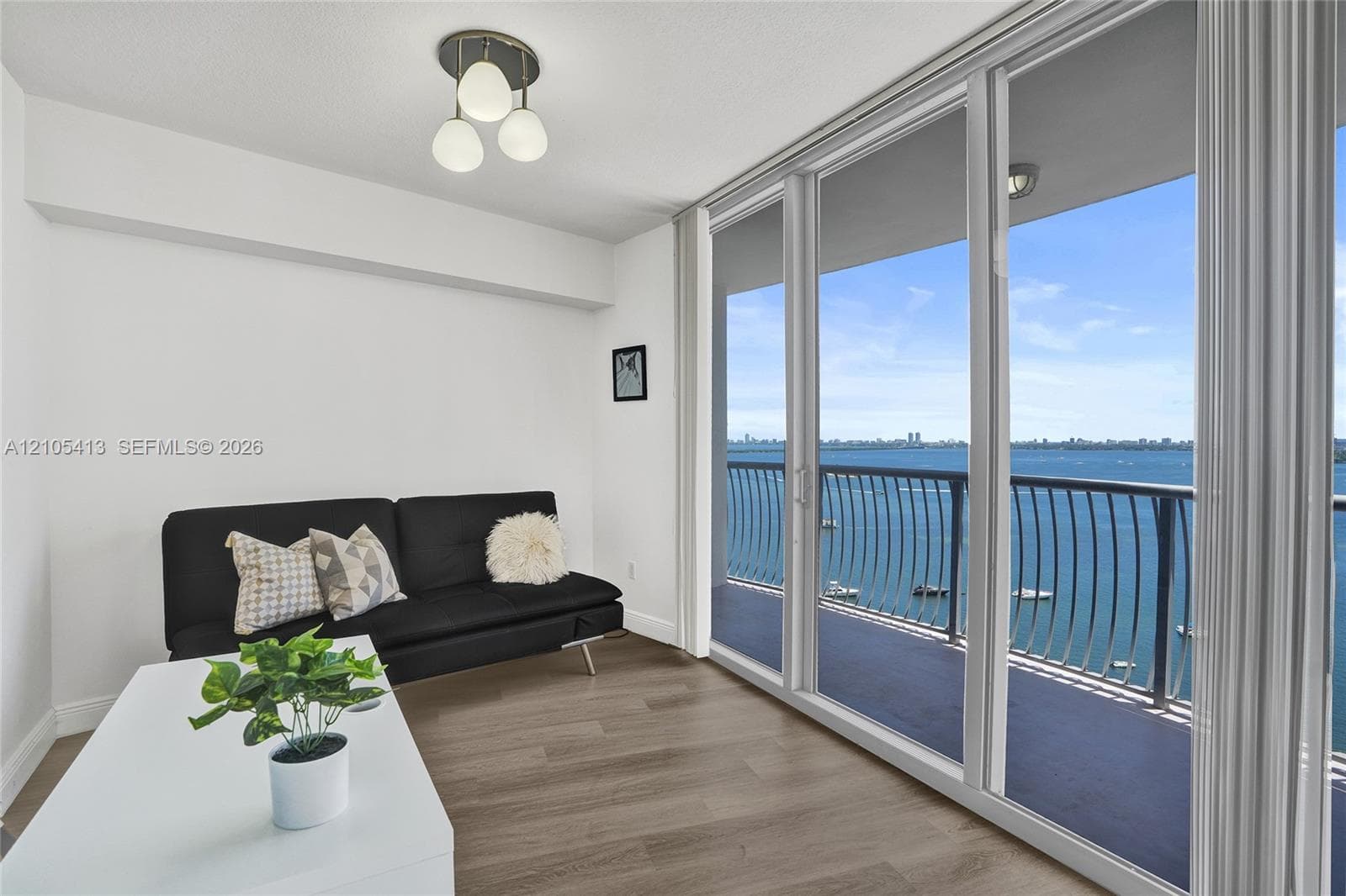 Expansive sliding glass doors, water scenery, balcony with metal railing, wood-finish flooring, and a contemporary semi-flush mount light fixture