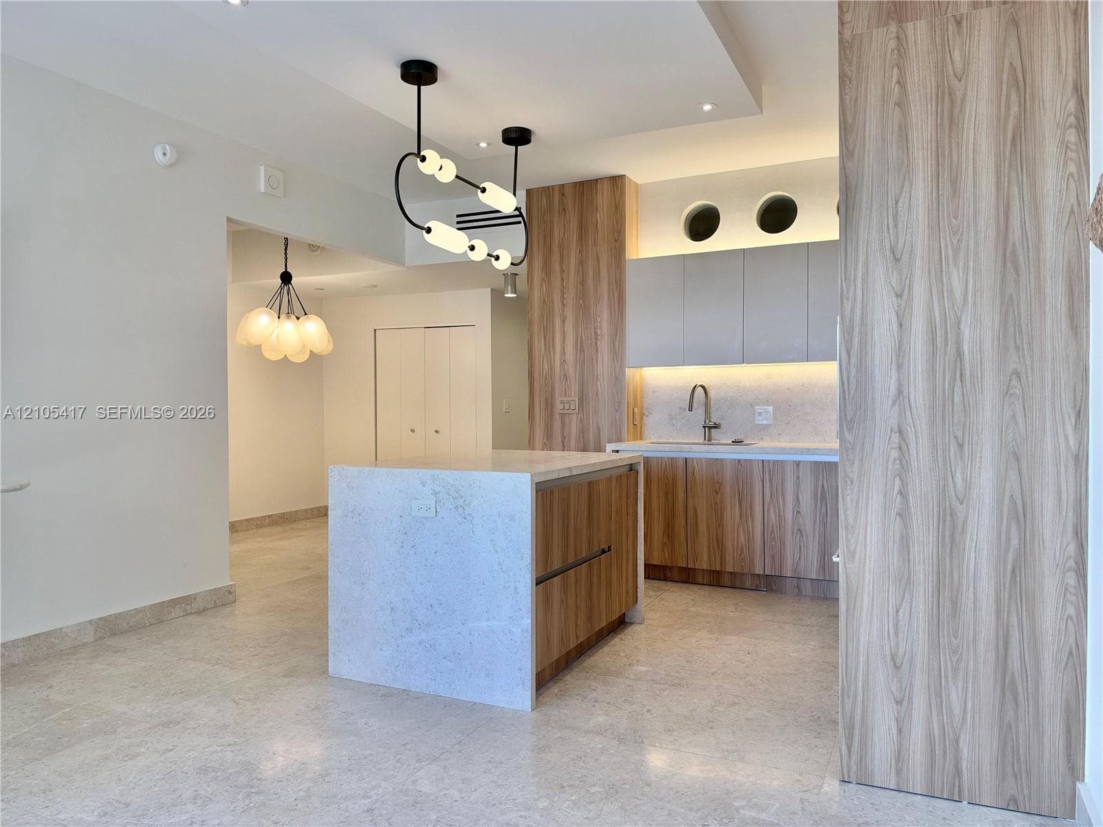 Kitchen featuring a central island with a stone countertop, wood-finish cabinetry, under-cabinet lighting, and a stainless steel sink with a gooseneck faucet