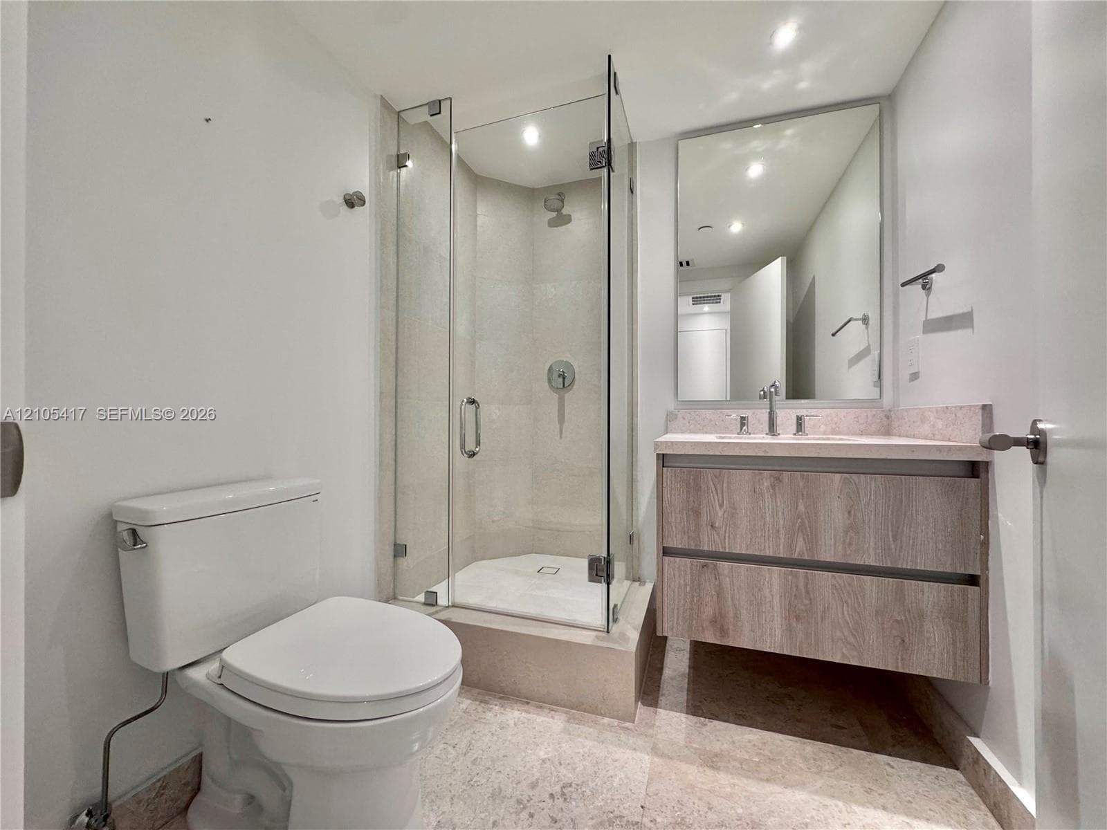 Glass-enclosed shower with a tiled interior, floating vanity with wood-finish cabinetry, and a framed mirror