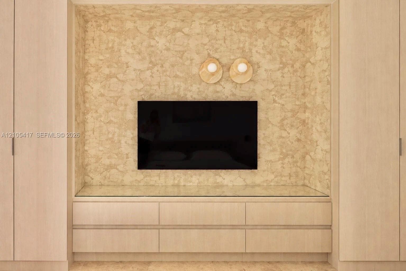 Integrated entertainment center with textured wall finish, wood-finish cabinetry, and glass countertop