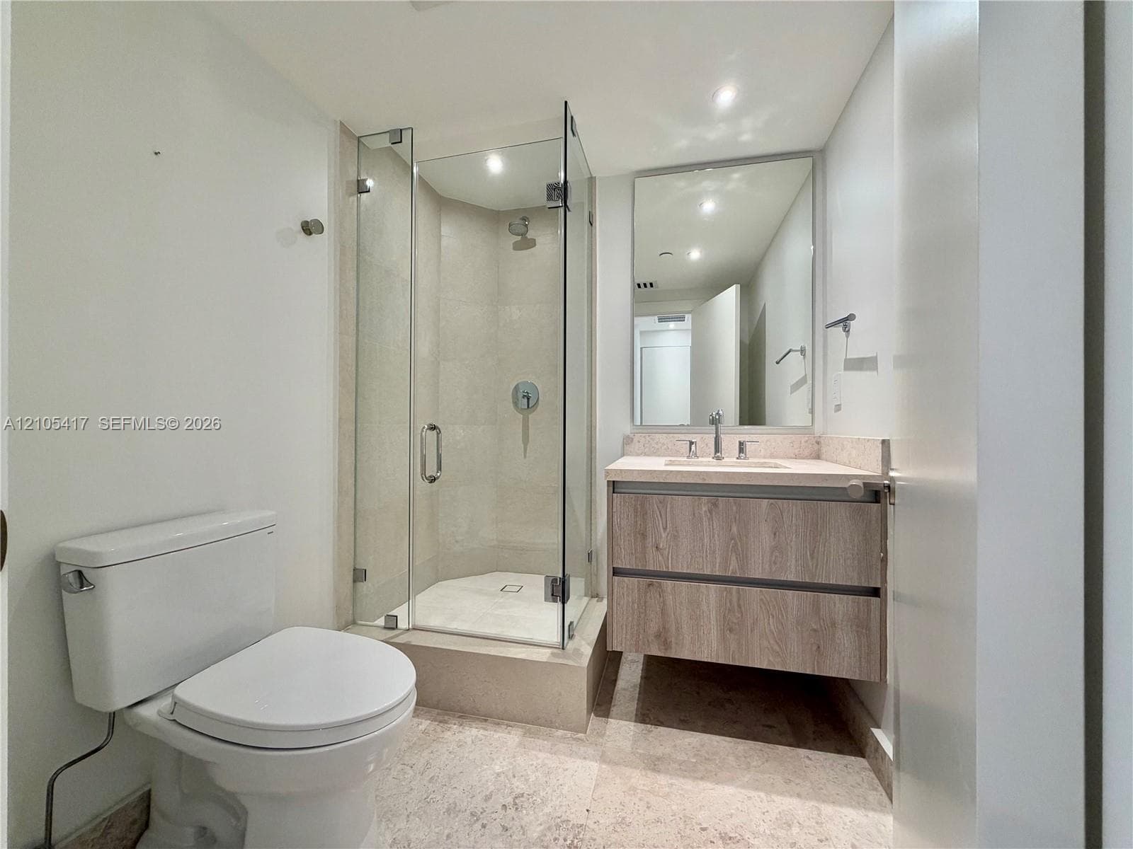 Walk-in shower with glass enclosure, floating wood-finish vanity, stone countertop with integrated sink, rectangular wall-mounted mirror, and tile flooring