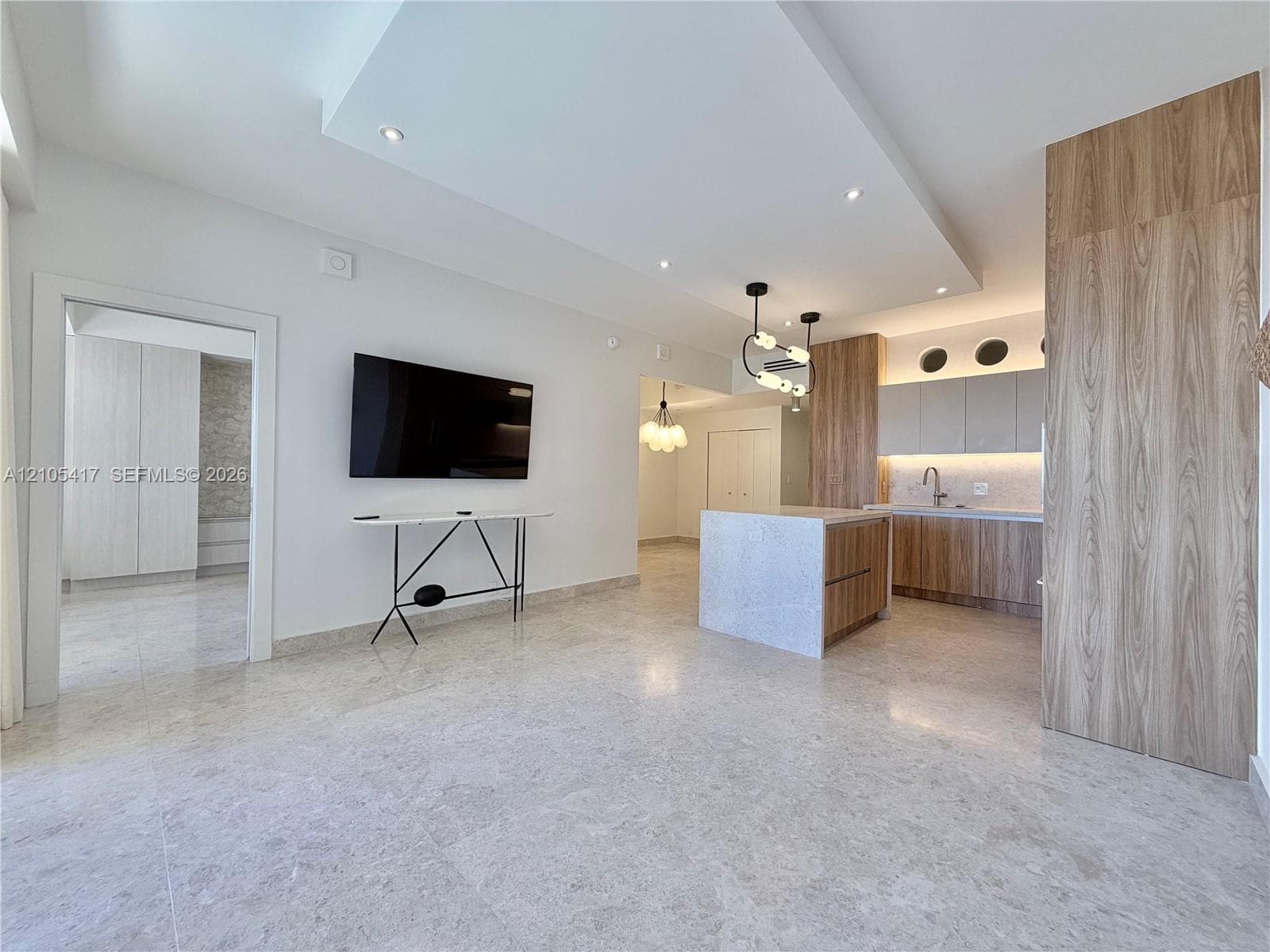 Recessed lighting, wood-finish cabinetry, a central kitchen island, light-toned tile flooring, and a contemporary pendant light fixture