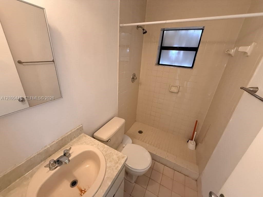 Bathroom featuring a vanity with an integrated sink, a wall-mounted mirror, a tiled shower enclosure, and a window