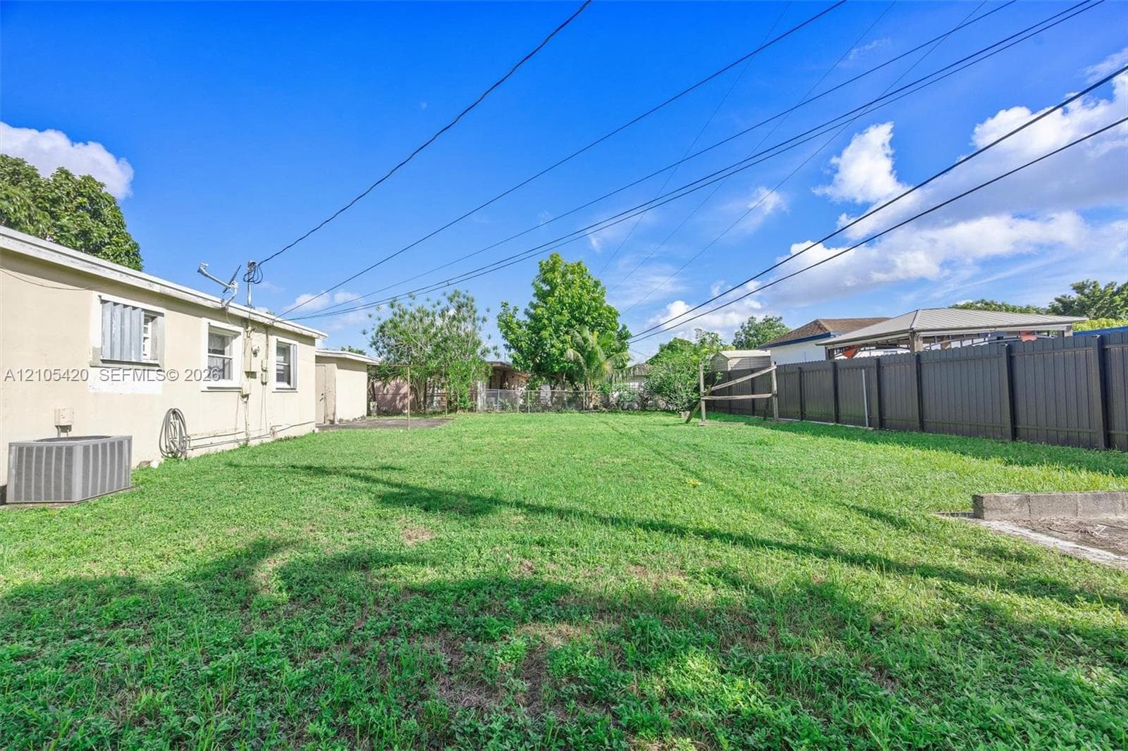 Expansive grass yard with a dark privacy fence and concrete slab