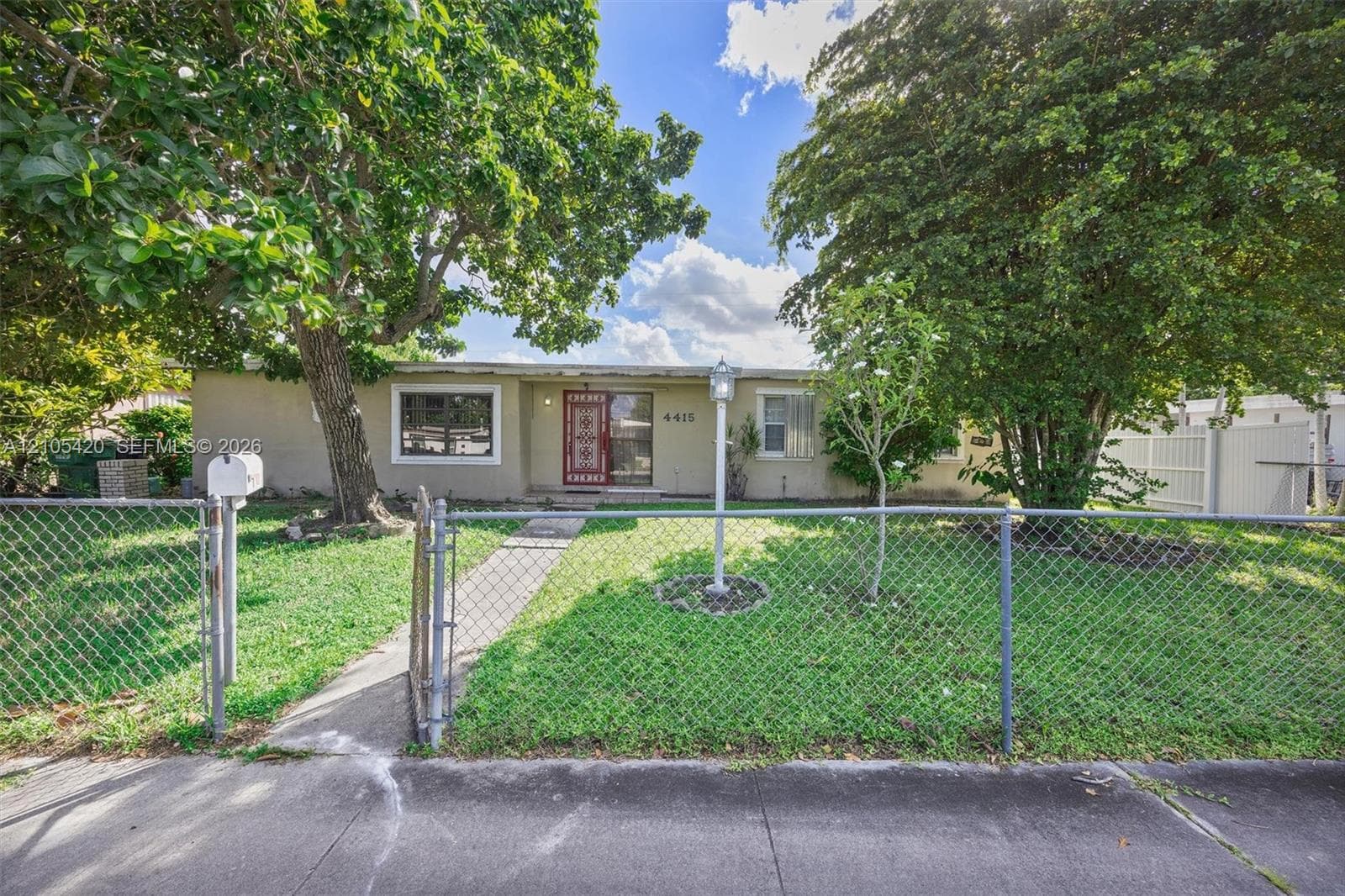 Single-story residence featuring a chain-link fence, concrete pathway, and mature trees