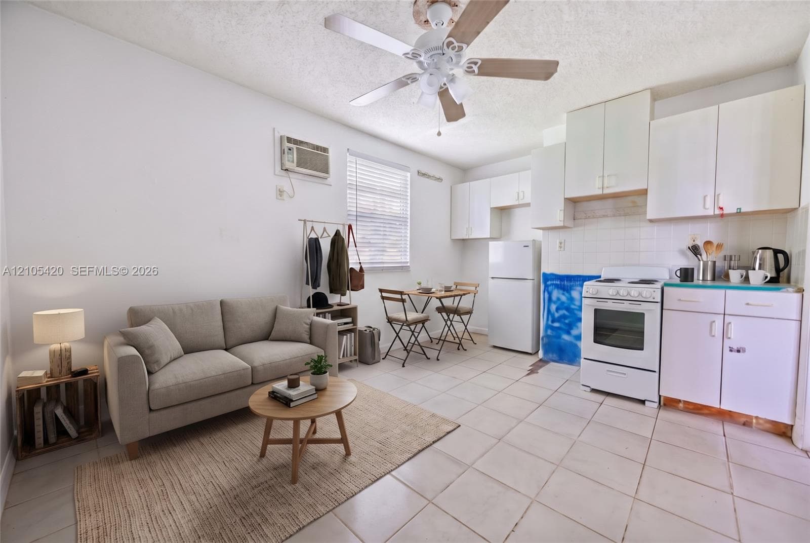 White kitchen cabinetry with a tile backsplash, ceiling fan, and window with blinds