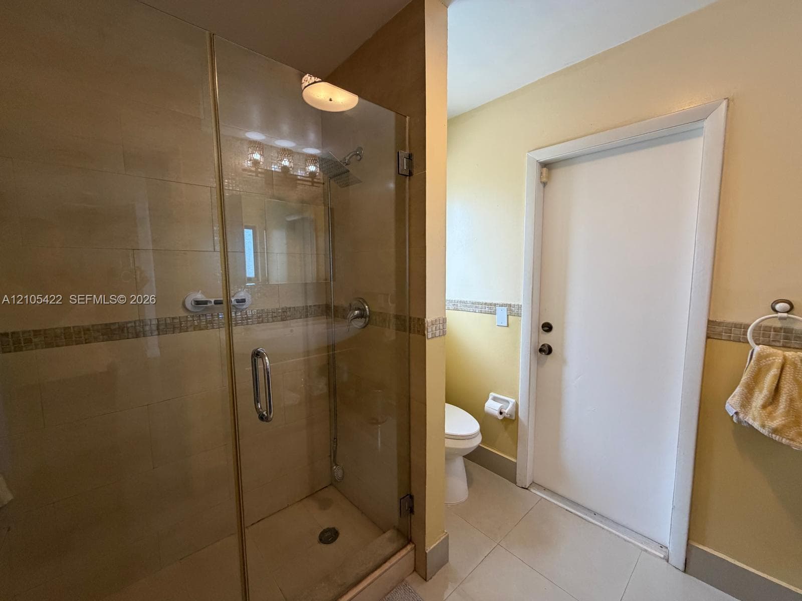 Walk-in shower with a glass enclosure, tile surround, decorative mosaic tile inlay, and integrated plumbing fixtures, featuring large-format tile flooring