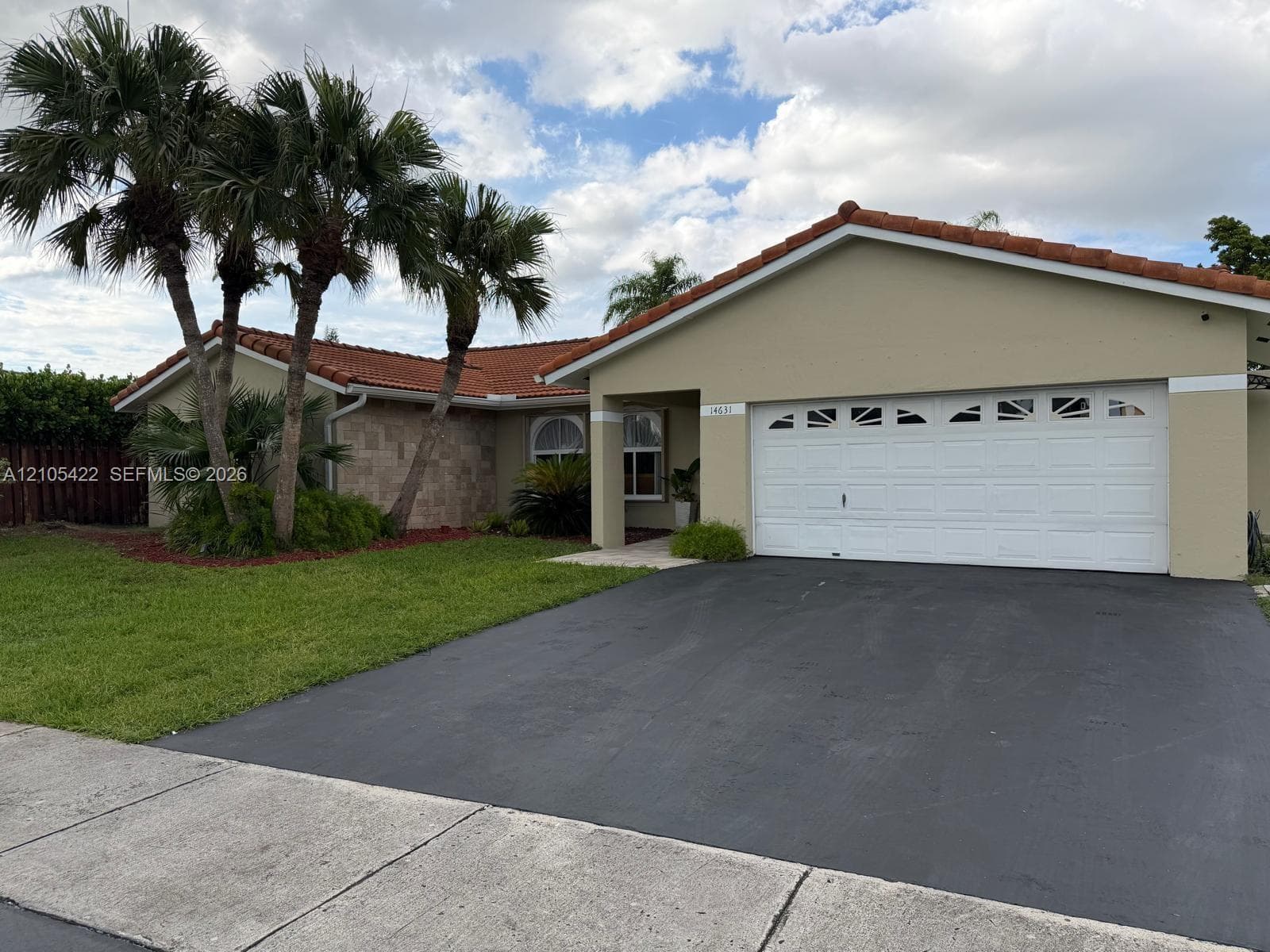 Exterior featuring a terracotta tile roof, beige stucco facade, stone-accented wall, arched window detailing, and a two-car garage