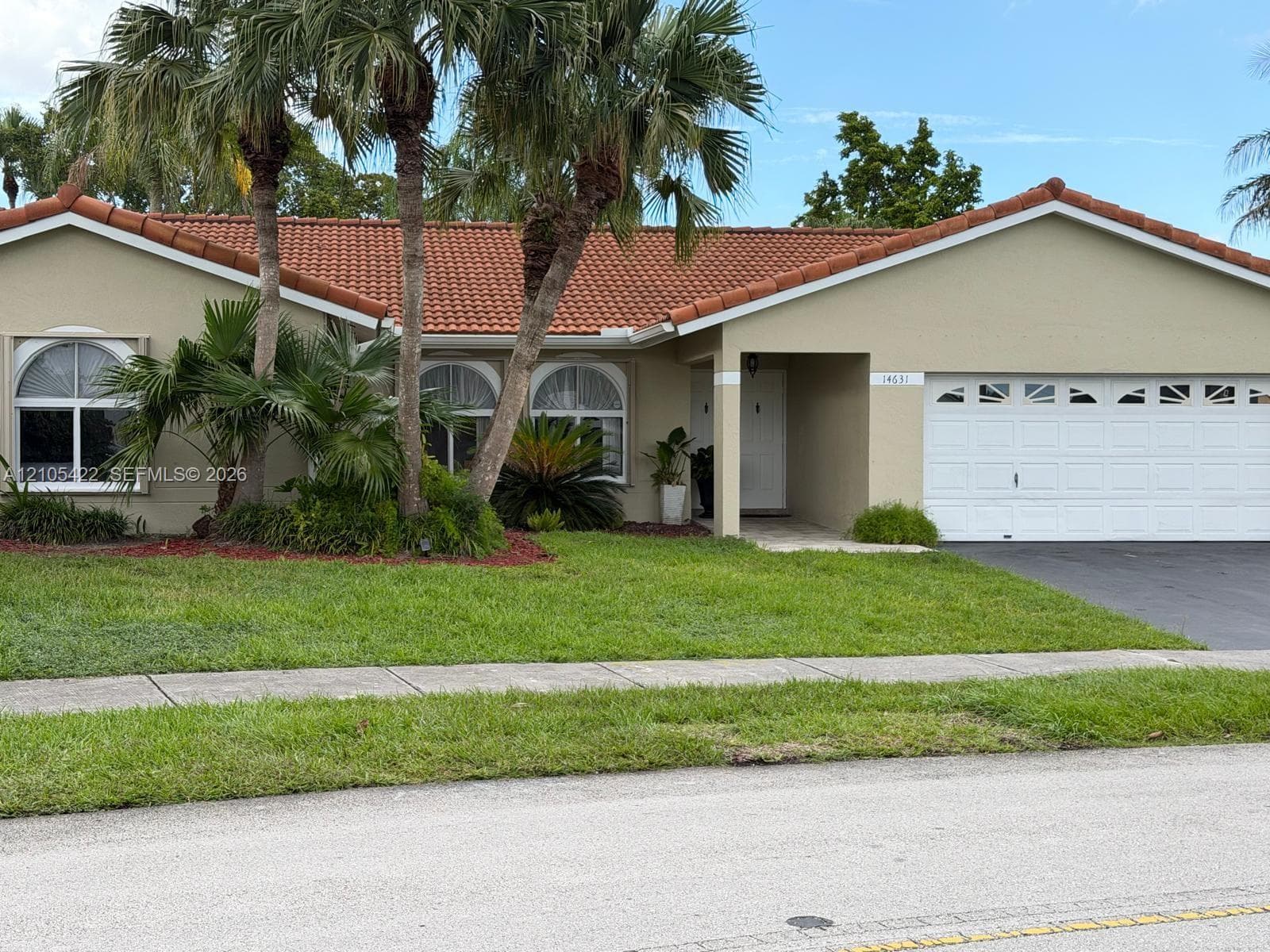 Single-story exterior featuring a clay tile roof, arched window accents, and a two-car garage