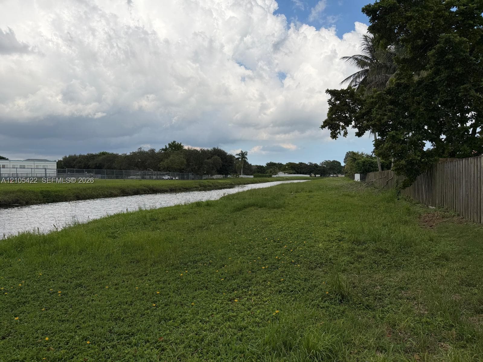 Waterfront parcel featuring open green space, mature trees, and wooden perimeter fencing