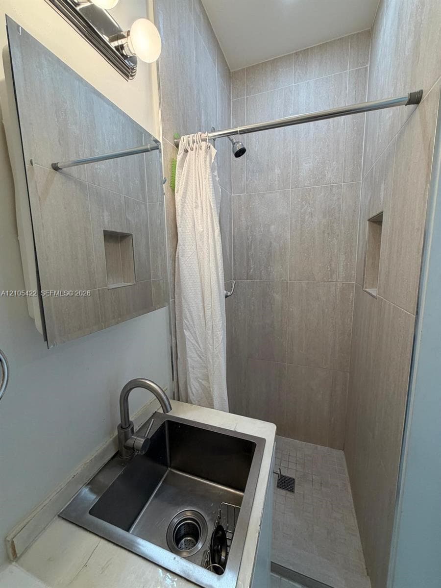 Bathroom featuring a square undermount sink with a gooseneck faucet, light-toned countertop, wall-mounted mirror, and a walk-in shower with neutral wall tiling and recessed shelving