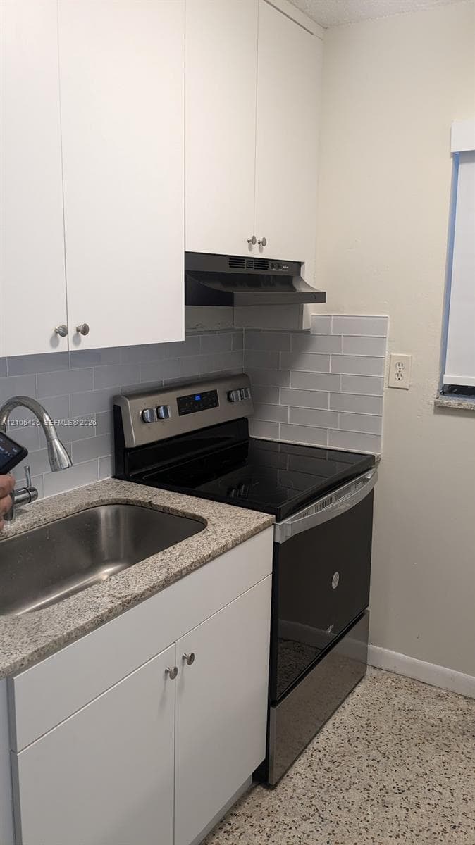 White upper and lower cabinetry, stainless steel sink with a gooseneck faucet, light-toned countertop, and a gray subway tile backsplash
