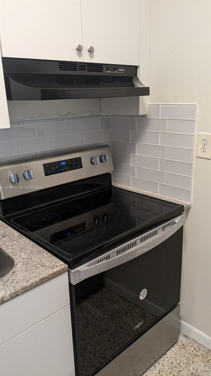 Stainless steel electric range with a smooth cooktop, complemented by light grey subway tile backsplash and a speckled countertop