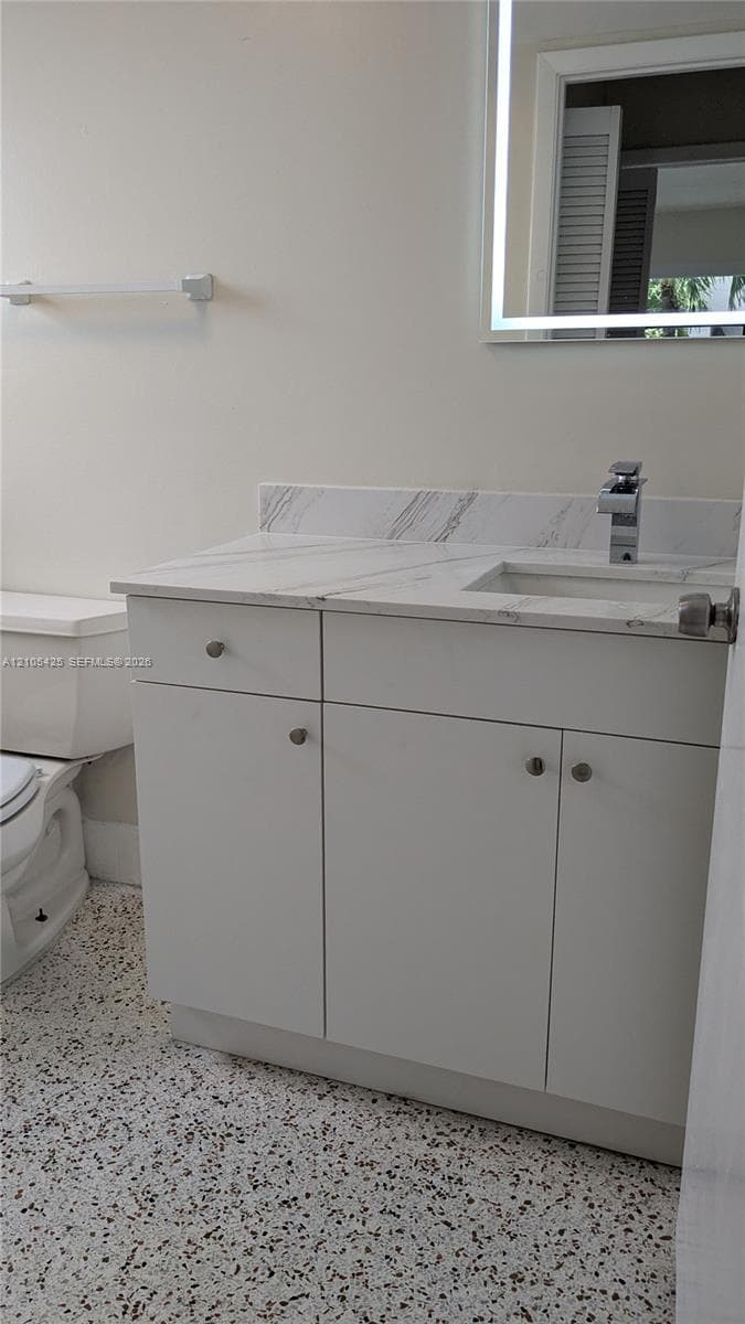 White vanity with a light-toned countertop, integrated sink, and a framed mirror with integrated lighting