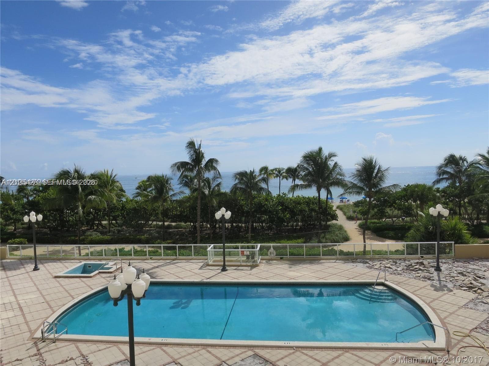 Outdoor swimming pool featuring a white deck, clear perimeter fencing, and mature palm trees