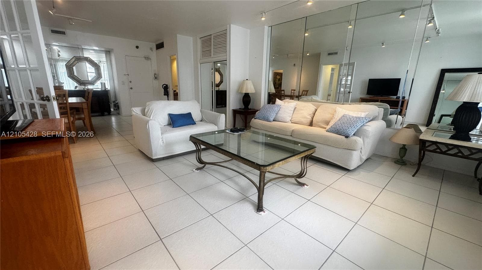Tile flooring, mirrored wall accents, track lighting, and a glass-top coffee table